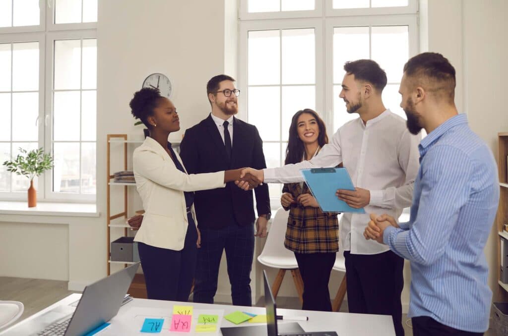 Team in einem Büro begrüßt einen Kollegen per Handschlag
