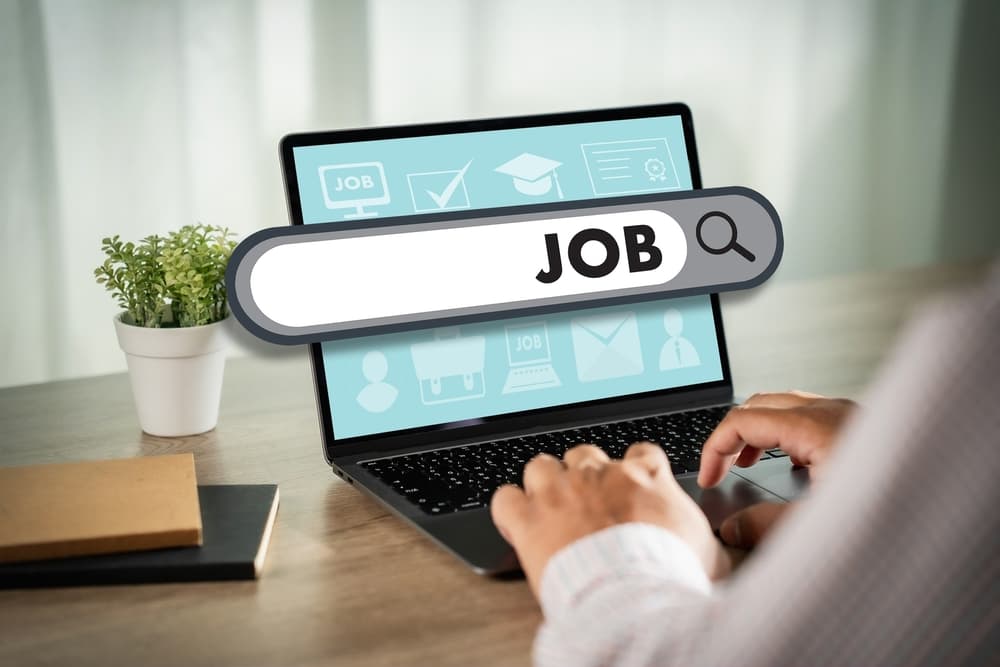Person tippt auf einem Laptop, darüber eine Suchleiste mit dem Wort „JOB“