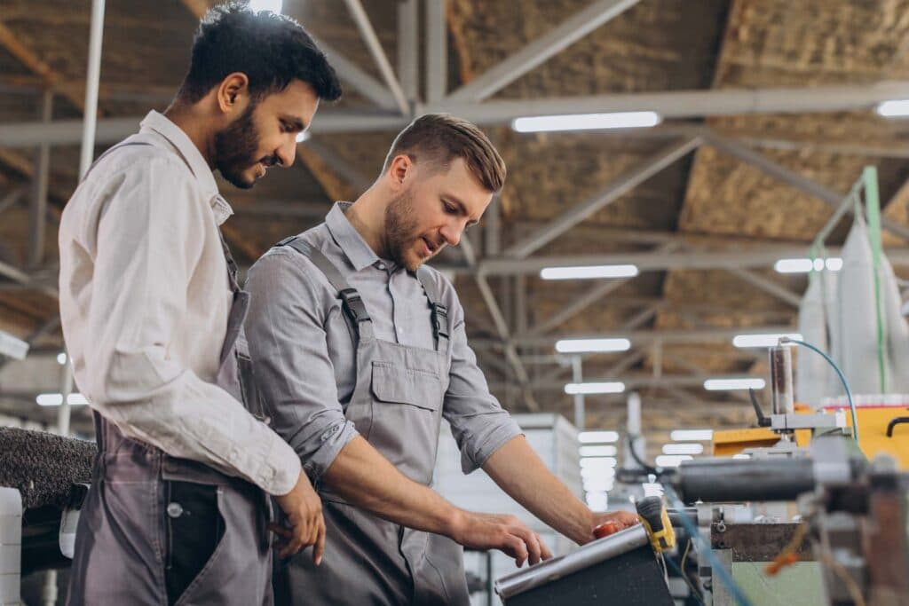 Zwei Handwerker in Arbeitskleidung an einer Maschine in einer Werkhalle